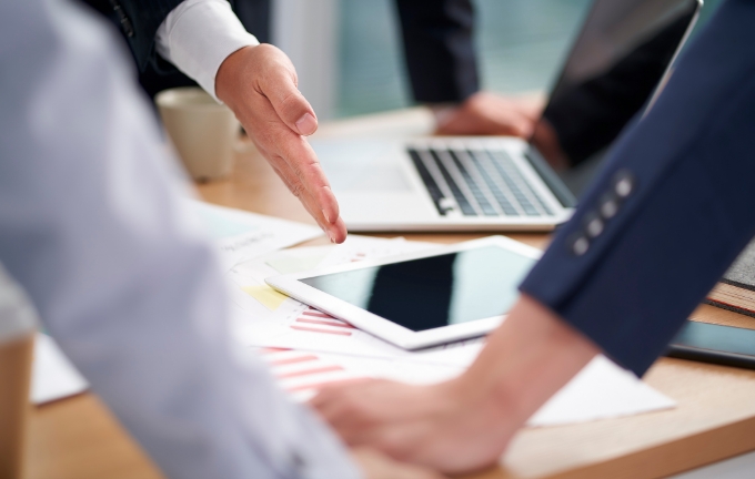 複数人がタブレットと資料を囲んで会議をしている様子。営業支援ツール「Tappo」の活用を想起させるイメージ。